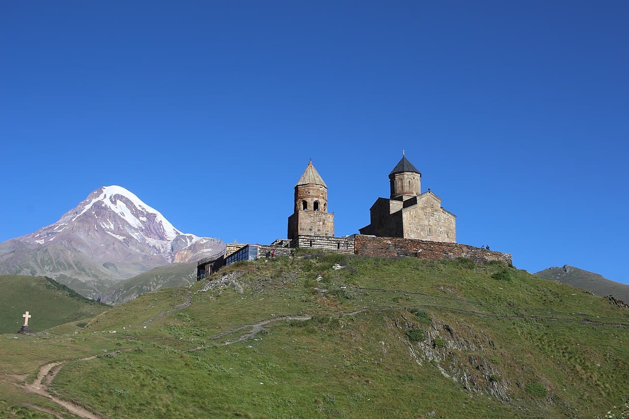 Gergeti Trinity Church on a grassy hill, with Mount Kazbek behind.